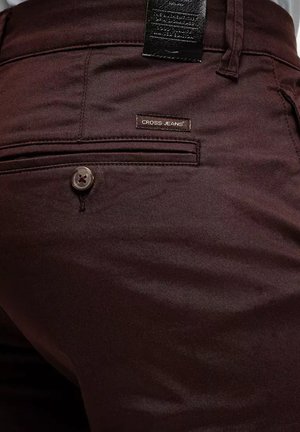 Brązowe spodnie wykonane z gładkiego materiału o delikatnym połysku. Posiadają metkę z napisem "CROSS JEANS" oraz okrągłe zapięcie na guzik.