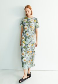 Blumendruckkleid aus weichem Stoff, mit kurzen Ärmeln und lockerem Schnitt. Die Farben umfassen Grün, Weiß, Orange und Lila, mit einer seitlichen Bindewelle.