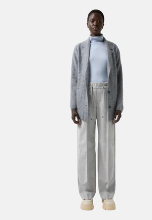 Grau fuzzy Cardigan über einem hellblauen Rollkragenpullover; graue weit geschnittene Hose mit Kordelzug; cremefarbene Plateausneaker.