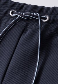 Navy blue textured fabric of shorts featuring a drawstring with silver eyelets and contrasting light blue accent threads.