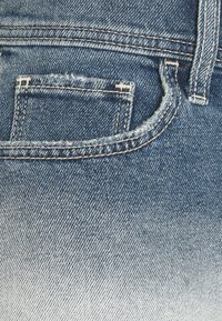 Džínové kalhoty v světle modré barvě s vybledlým gradientem, viditelným šitím, zadní kapsou a mírně opotřebovanou texturou.