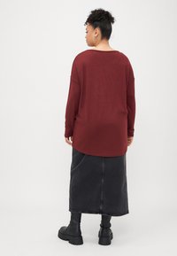 Top de manga longa vinho com um decote arredondado, combinado com uma saia de ganga preta e botas pretas chunky até ao tornozelo. Textura de tecido suave.