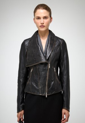 Giacca in pelle nera con ampio colletto, zip frontale asimmetrica, due zip laterali e finitura testurizzata. Il design presenta cuciture pronunciate.