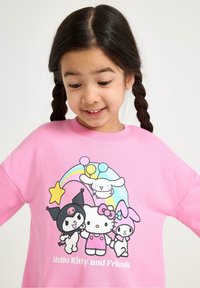 Vaaleanpunainen collegepaita, jossa on graafinen kuva Hello Kittystä ja hänen ystävistään, värikkäillä yksityiskohdilla, sateenkaari ja leikkisiä hahmosuunnitelmia.