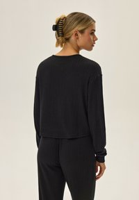 Czarny, prążkowany top z długim rękawem, charakteryzujący się luźnym krojem, okrągłym dekoltem i opadającymi ramionami, zestawiony z dopasowanymi spodniami dla uzyskania spójnego wyglądu.