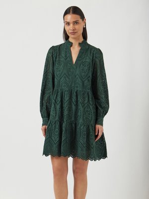 Robes vertes en tissu tissé avec des détails en broderie anglaise, manches longues et ourlet en forme de vagues. Décolleté en V et design de jupe à volants.
