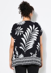 Schwarze Bluse mit weißem Blattmuster, kurzen Ärmeln und dekorativem Saum. Hergestellt aus leichtem Stoff, mit lockerer Passform.
