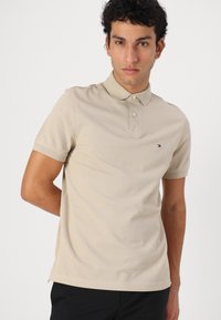 Beige bomulds polo shirt med tre-knaps placket, korte ærmer og et lille logo på brystet. Glat tekstur, afslappet pasform.