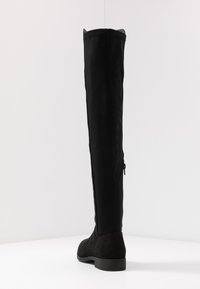 Botte noire au-dessus du genou avec une tige en textile lisse, une partie inférieure en suede, un bout rond et un talon fin, avec une fermeture éclair sur le côté.