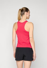 Rdeča športna majica brez rokavov z obliko racerback, v kombinaciji z črnimi kratkimi hlačami. Tkanina izgleda gladka in lahka.