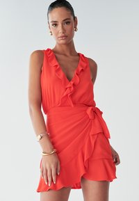 Rode jurk met ruffle halslijn en gelaagde zoom, met een strikdetail bij de taille. Gemaakt van lichte stof met een zachte textuur.