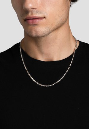 Sølv kæde med et geometrisk linkdesign, båret over en sort t-shirt, med en glat, reflekterende overflade og subtil tekstur.