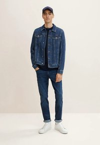 Teksariidest jakk nööpidega, kahe rinnataskuga. Sügavsinised teksad ja valged tossud lõpetavad komplekti. Peal sirge tumesinine T-särk.