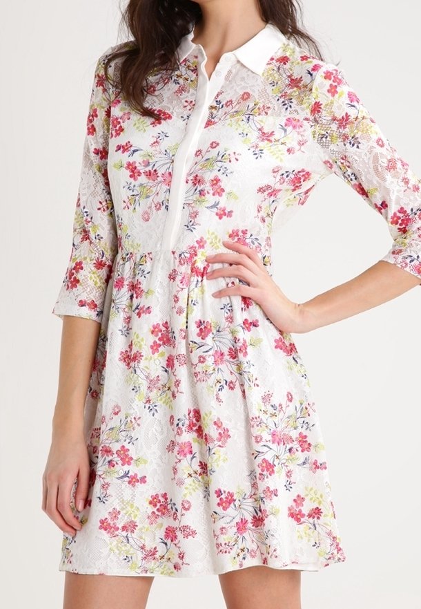 Robe fleurie courte avec une base blanche, ornée de motifs floraux roses, jaunes et verts, avec un col et des manches trois-quarts.