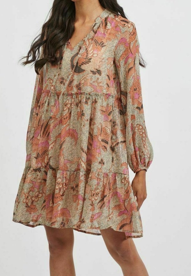 Femme portant une robe longueur genou à manches longues, à motif floral avec un ourlet à volants superposés dans des tons de rose, marron et beige.