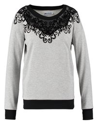 Sweat-shirt gris clair à manches longues avec poignets et ourlet côtelés noirs, avec dentelle noire et motifs tourbillonnants brodés autour de l'encolure.