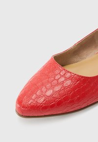 Chaussure plate rouge texturée avec un bout pointu et une doublure intérieure beige sur fond blanc.