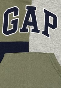 Mikina s kapucňou GAP s farebným blokovým dizajnom; obsahuje olivovú, námornícku a šedú bavlnenú tkaninu; veľké vyšívané logo "GAP" v námorníckej farbe.