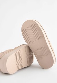 Scarpe con plateau di un beige chiaro, caratterizzate da una suola in gomma testurizzata con un motivo a zig zag e un materiale superiore liscio con dettagli di cucitura sottili.