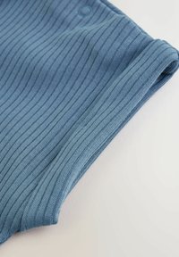 Blå ribbad tyg med en mjuk textur, med en rullad fåll och en liten knappdetalj nära överkanten.