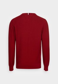 Red knit sweater with a textured diamond pattern, long sleeves, ribbed cuffs, and a v-neck. Features a striped accent at the back neck.
