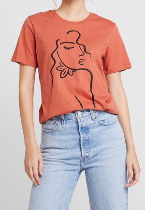 Frau trägt rostfarbenes T-Shirt mit schwarzer durchgehender Linienzeichnung eines Frauenkopfes, kombiniert mit hellblauen High-Waist-Jeans.