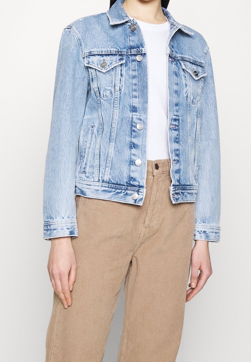 Ljusblå denimjacka med krage, framfickor och silverfärgade knappar. Buren över en vit skjorta och matchad med beige kordflorsbyxor.