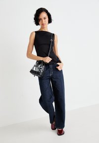 Zwarte mouwloze top, brede donkere denim broek en glanzende zwarte handtas. Bordeaukleurige schoenen met een gladde afwerking maken de look compleet.