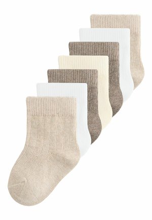Syv par ribstrikkede babysokker i beige, hvid, creme og lys brun, arrangeret i et forskudt overlappende layout.