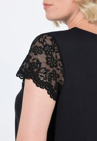 Top nero con maniche corte realizzato in pizzo floreale con bordi scallop, abbinato a un morbido tessuto nero uniforme.