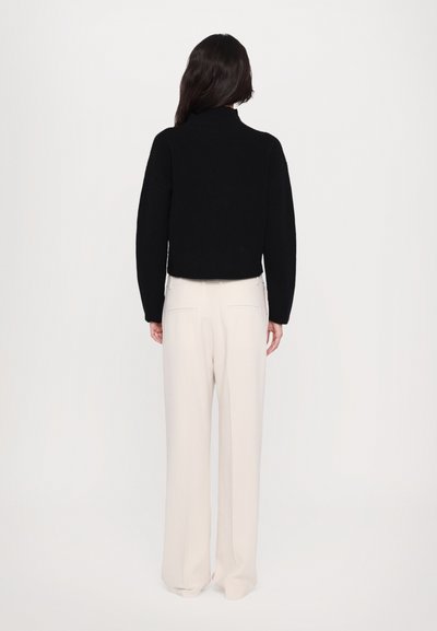 Black cropped sweater with a high neck, textured fabric, paired with beige wide-leg trousers, featuring pockets and a smooth finish.