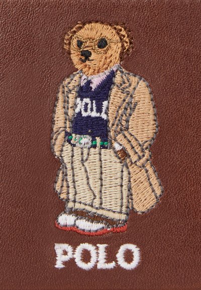 Embroidered bear wearing a beige suit over a navy sweater with "POLO," standing on a brown background, red and white sneakers below.
