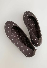 Brązowe płaskie buty z białymi kropkami, zaokrąglonym noskiem, odsłoniętymi bokami oraz teksturowanym wnętrzem z mniejszymi białymi kropkami. Podeszwa z gumy i gładkie wykończenie.