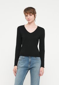 Zwarte longsleeve V-hals top in ribbelstof met een ruwe zoom, gecombineerd met lichtblauwe jeans, met een relaxte pasvorm en een eenvoudig ontwerp.