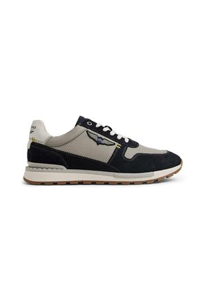 Low-top sneaker in beige and black with white laces, textured fabric, suede details, winged emblem on side, and rubber sole.