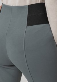 Pantaloni grigi elasticizzati con un alto bordo nero in vita, realizzati in un tessuto liscio e morbido e con un design aderente. Le cuciture visibili esaltano la silhouette.