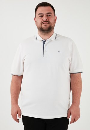 Cămașă polo albă cu guler și margini bleumarin, având o închidere cu trei nasturi și un logo brodat pe piept. Mâneci scurte.