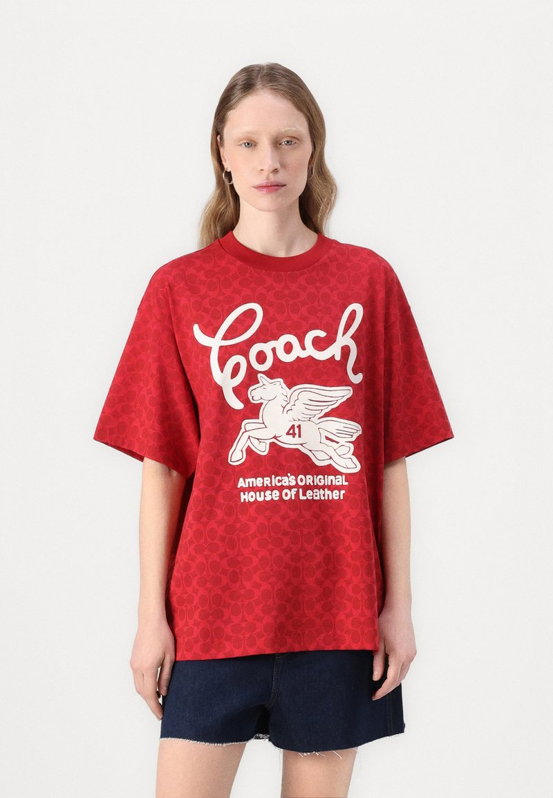 T-shirt vermelha com um corte oversized, mangas curtas e padrão texturizado; impressão gráfica branca com um cavalo alado e o nome da marca.