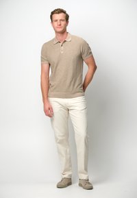 Beige short-sleeve polo shirt with two-button placket, paired with off-white trousers and light beige sneakers, all featuring a smooth texture.