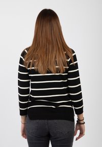 Maglione a righe bianche e nere con maniche lunghe e orlo a coste, indossato sopra jeans scuri, vista posterior. Texture liscia.