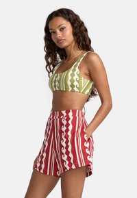 Haut de bikini à motifs verts et blancs avec un décolleté dégagé, associé à un short rayé rouge et blanc avec des motifs ondulés et des poches latérales.