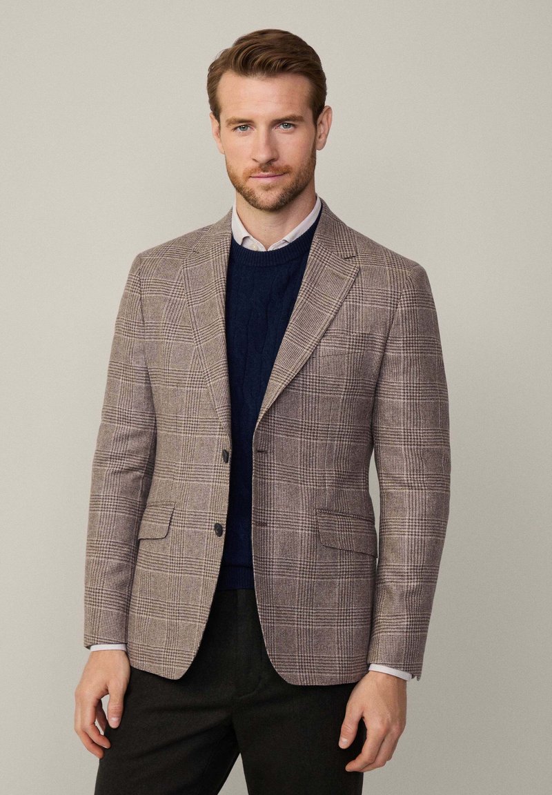 Hnědý kostkovaný blazer s klopami, dvěma knoflíky a bočními kapsami. Nosený přes námořnický svetr s texturovaným pleteným vzorem.