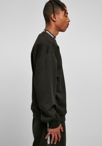 Sort sweatshirt med rund hals, ribbede manchetter og "STARTER" logo på kraven. Stoffet ser blødt ud med en let struktureret overflade.