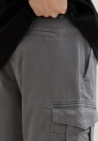 Gray cargo pants made of durable fabric, featuring pockets, textured surface, and subtle stitching details. Cuffs show practical, functional design.