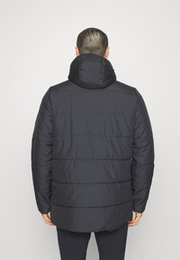 Giacca a vento nera con colletto alto, caratterizzata da un design trapuntato e bordi a costine. Il materiale sembra liscio e isolato.