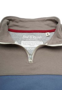 Barntröja med brun krage, blå kropp, halv dragkedja och etikett som visar märke, storlek 110/116 och certifierad ekologisk bomull.