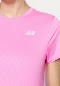Pink athletic t-shirt with short sleeves, featuring a textured fabric and a small white New Balance logo on the left side.