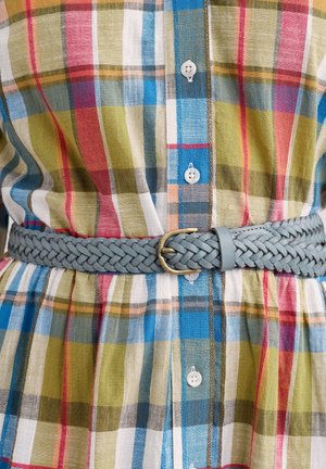 Chemise en tartan aux couleurs vives : vert, bleu, rouge et blanc. Accompagnée d'une ceinture en cuir tressé gris clair avec une boucle en or.