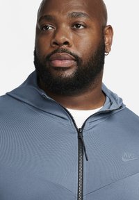 Gray zip-up hoodie with a hood, featuring smooth texture, black accents, and a small Nike logo on the chest.