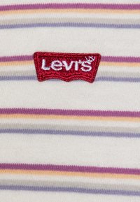 Stripet bomuldsstof med skiftende lilla, orange og grå striber på en lys cremefarvet baggrund. Rød broderet Levi's-logo patch.
